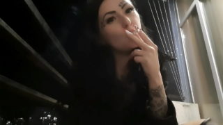 A senhora Nika fuma sexy à noite na varanda e sopra fumaça na sua cara.